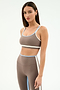 A woman stands against a plain light background, wearing the SPLITS59 Eva Rigor Double Strap Bra in Lentil/White with matching high-waisted leggings featuring light blue and white trim.