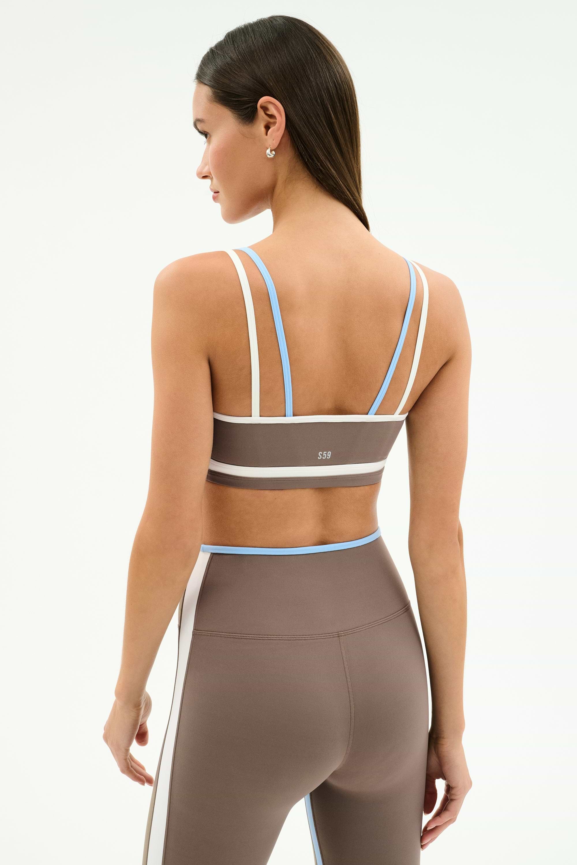 Woman wearing the SPLITS59 Eva Rigor Double Strap Bra in Lentil/White with matching high-waisted leggings, standing with her back to the camera—ideal as a yoga or workout bra for an active lifestyle.