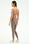 A woman stands in profile wearing the SPLITS59 Eva Rigor Double Strap Bra in Lentil/White, paired with matching high-waisted leggings and white sneakers.