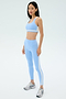A woman stands on a plain background wearing the SPLITS59 Miles High Waist Rigor 7/8 leggings in Skylight/White and a matching sports bra, paired with silver athletic shoes.