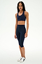 A woman stands against a plain white background wearing the SPLITS59 Sara Airweight Bra in Indigo, paired with matching high-waisted, knee-length leggings and white sneakers—an ideal outfit for hot yoga or Pilates sessions.