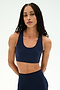 A woman with long braided hair stands against a plain white background, looking directly at the camera with a neutral expression, modeling the SPLITS59 Sara Airweight Bra in Indigo and matching leggings—perfectly poised for hot yoga or Pilates.