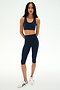 A woman wearing the SPLITS59 Sara Airweight Bra in Indigo with matching knee-length leggings and white sneakers, standing against a plain white background—an ideal outfit for hot yoga or Pilates sessions.