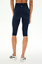 A person is wearing SPLITS59 Airweight High Waist 16" Capri Legging in Indigo and white sneakers, standing on a white background, viewed from the back.