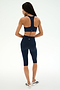 A woman stands facing away, wearing the SPLITS59 Sara Airweight Bra in Indigo and matching high-waisted biker shorts—ideal for Pilates or hot yoga—paired with white athletic shoes, set against a plain light background.