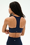 A woman with braided hair wears the SPLITS59 Sara Airweight Bra in Indigo and matching leggings, standing with arms crossed and facing away from the camera—perfectly dressed for hot yoga or Pilates.