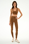 A woman wears the SPLITS59 Sara Airweight Bra - Toffee with matching high-waisted leggings and beige sneakers, standing against a plain white background.