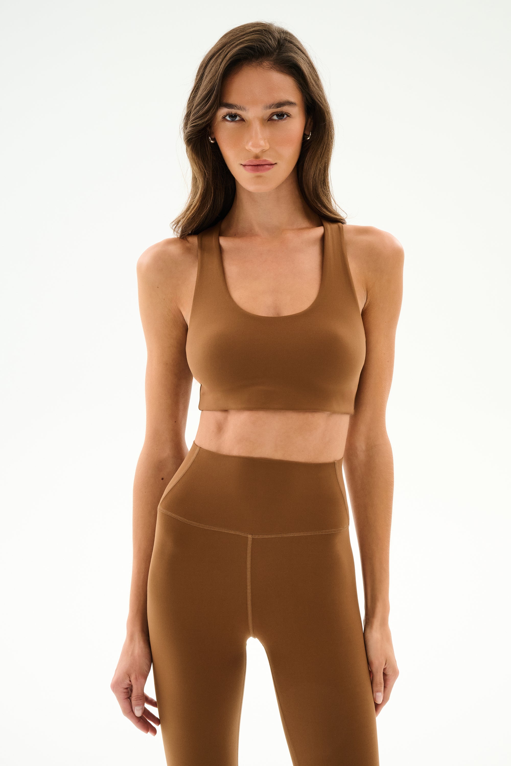 A woman faces forward wearing the SPLITS59 Sara Airweight Bra - Toffee and matching leggings, long hair down, neutral expression. Plain white background. HTS 6109.90.1090.