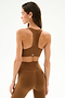 A woman wears the SPLITS59 Sara Airweight Bra - Toffee, facing away and looking to the side against a plain white background.
