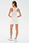 A woman faces away, wearing the SPLITS59 Venus High Waist Rigor Skort in white with a sleeveless top, white socks, and sneakers against a plain light background.