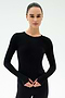 A woman with dark hair tied back wears the SPLITS59 Airweight Lite Long Sleeve Waist Length top in black, paired with black pants and posed against a plain white background—perfect for gym workouts.