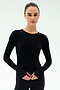 A woman with dark hair tied back wears the SPLITS59 Airweight Lite Long Sleeve Waist Length top in black, paired with black pants and posed against a plain white background—perfect for gym workouts.
