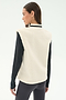 A woman stands with her back to the camera, wearing the SPLITS59 Aster Sherpa Vest in Creme over a black long-sleeve top and dark leggings.