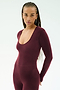 A person with long braids wears the SPLITS59 Chloe Airweight Jumpsuit in Dark Cherry, a fitted long-sleeve piece, standing against a plain light background.