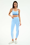 A woman stands against a plain background wearing the SPLITS59 Sam High Waist Rigor 7/8 leggings in Skylight/Cobalt, paired with a light blue sports bra and silver sneakers.