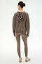 A person stands facing away, dressed in the SPLITS59 Joey Fleece Hoodie in Lentil—a brown hooded sweatshirt crafted from a soft modal spandex blend—paired with matching leggings and beige sneakers with stripes, set against a plain light background.