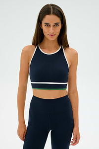 A person is standing against a plain background, wearing the Layla Airweight Bra in Indigo/White by SPLITS59, paired with navy blue leggings.