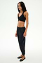 A person stands against a plain background wearing a black crop top, black SPLITS59 Megan Woven Nylon Jogger pants with a cinched waistband, and black ballet flats.
