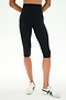 A person is shown standing in a studio, dressed in SPLITS59 Airweight High Waist 16" Capri Legging in black and wearing white sneakers with black accents, photographed from waist to feet.
