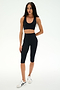 A woman stands against a plain white background wearing the SPLITS59 Sara Airweight Bra in black, paired with high-waisted black bike shorts and white sneakers—an ideal outfit for Pilates or hot yoga.