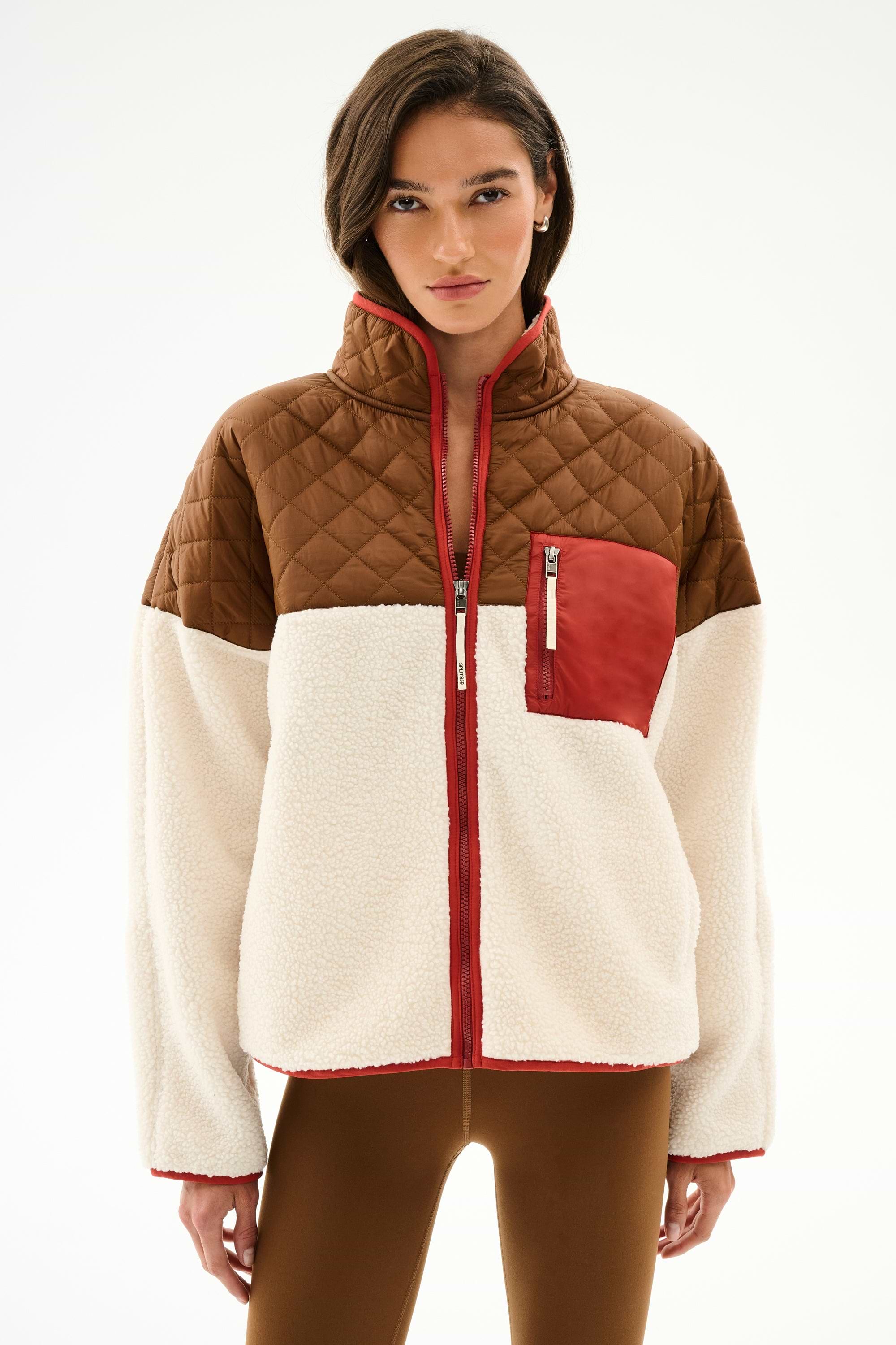 Woman wearing the SPLITS59 Skylar Sherpa Jacket - Creme/Toffee, featuring brown, cream, and red quilting with a zippered chest pocket, against a white background.
