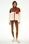 A woman stands against a white background wearing the SPLITS59 Skylar Sherpa Jacket - Creme/Toffee, brown leggings, and beige sneakers.