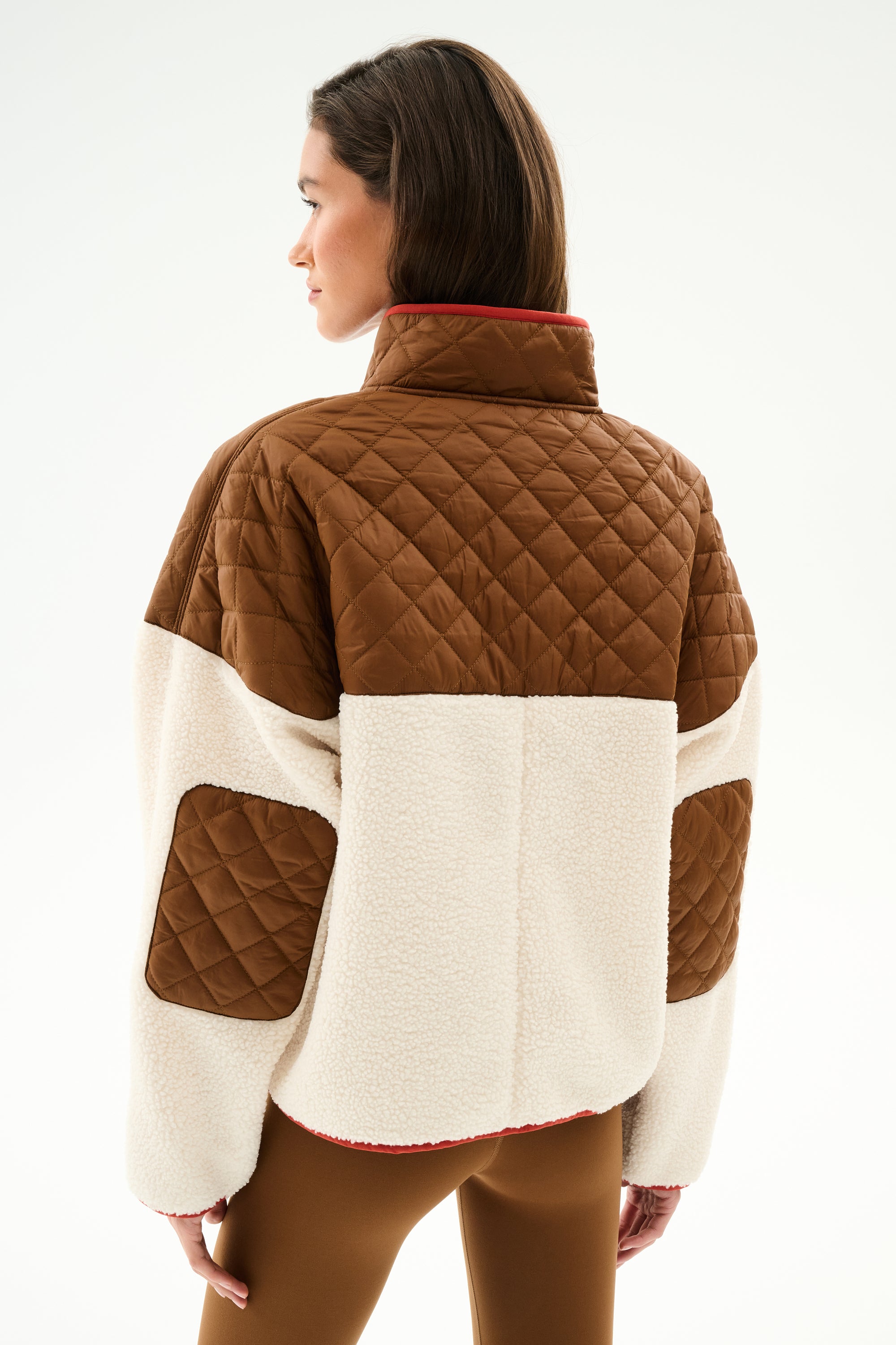 Woman facing away in the SPLITS59 Skylar Sherpa Jacket - Creme/Toffee, a 100% polyester quilted piece with high collar, paired with matching brown pants.