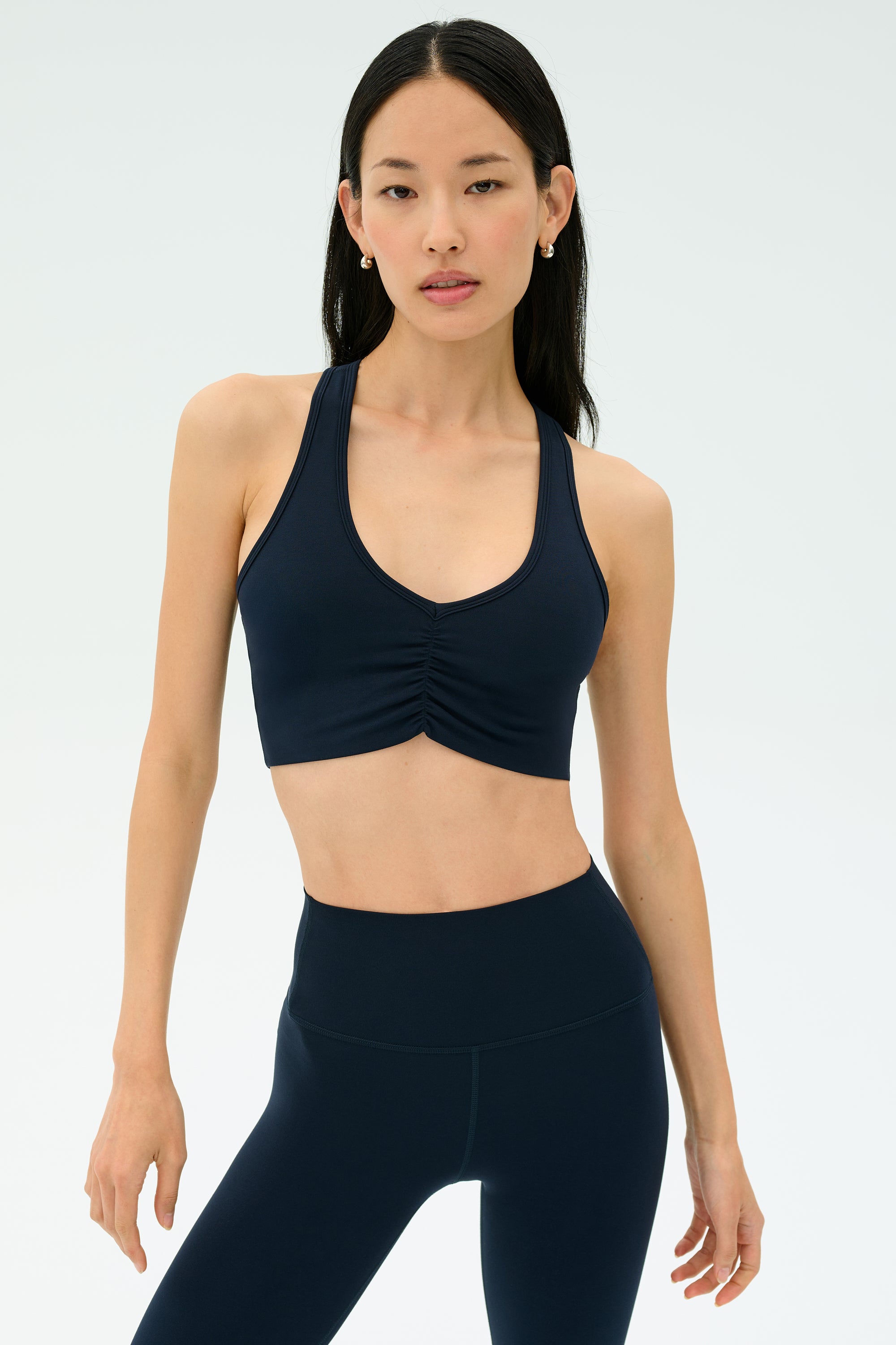A woman wearing the SPLITS59 Airweight Bra with Ruching in Indigo stands against a plain light background.