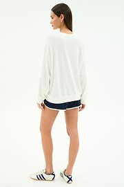 A person stands on a white background, facing away, wearing the SPLITS59 Andie Oversized Fleece Varsity Graphic Sweatshirt in white. This casually refined look is made in Los Angeles.