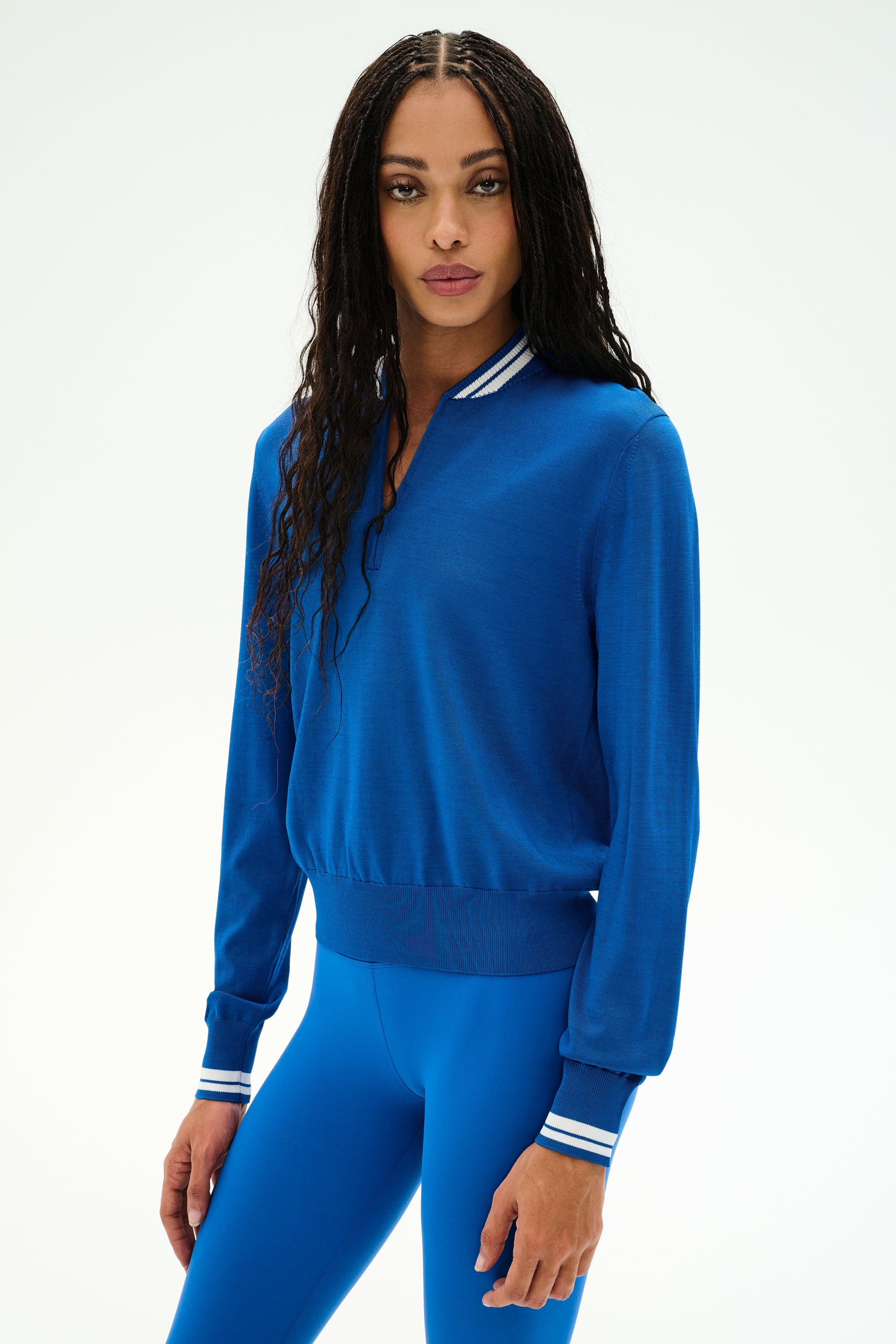 Wearing the SPLITS59 Bonnie Knit Half Zip in Classic Blue/White, a person stands facing forward against a plain white background, showcasing the blue long-sleeve top with white-striped cuffs and collar, paired with matching blue leggings. The outfit is crafted from soft rayon.