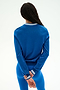 A person with long dark hair stands facing away, wearing the SPLITS59 Bonnie Knit Half Zip in Classic Blue/White paired with matching blue leggings, holding one wrist behind their back against a plain light background.