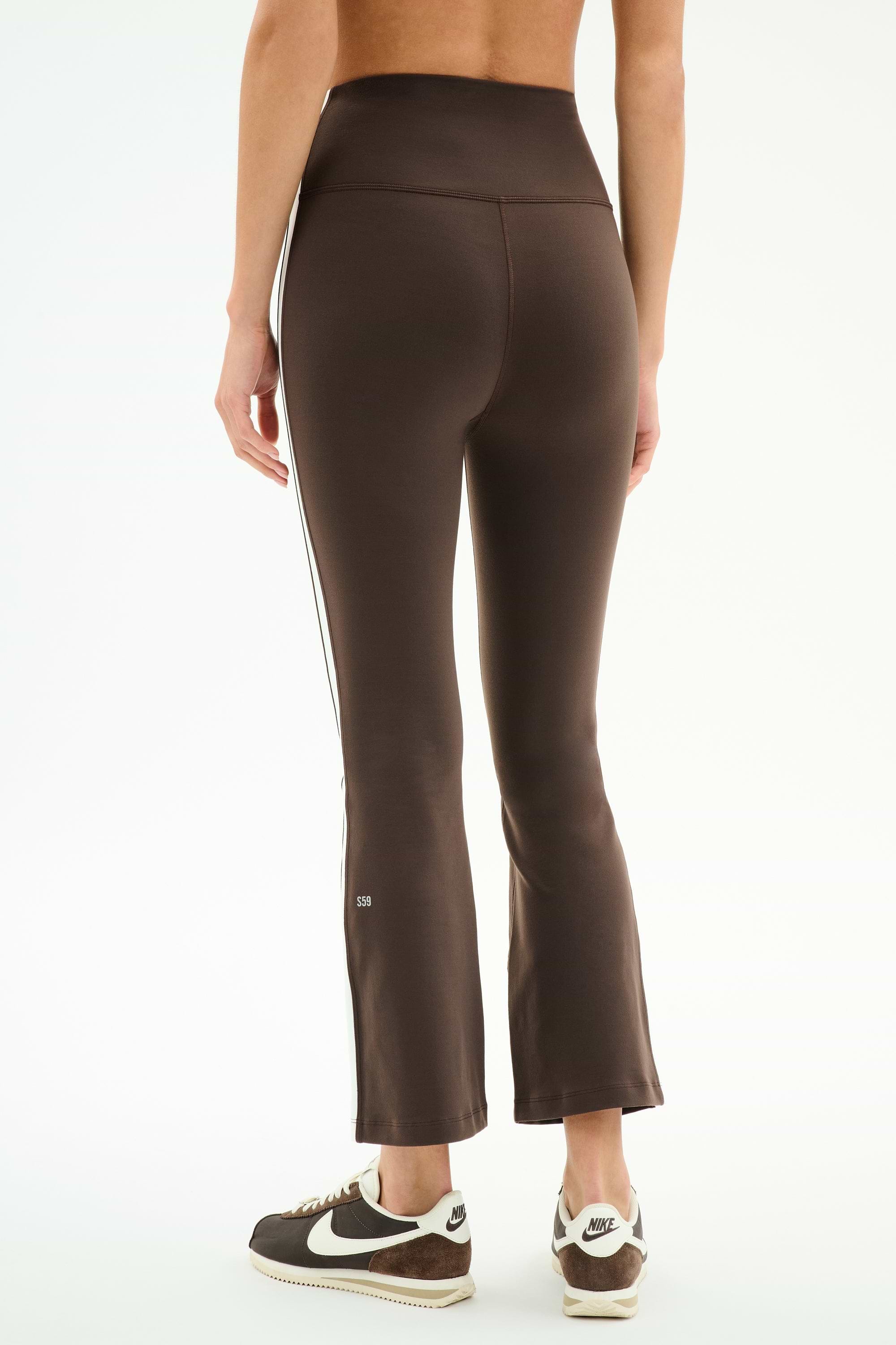 Someone wearing SPLITS59 Raquel High Waist Supplex Crop leggings in Dark Chocolate/White and black-and-white Nike sneakers, shown from the back against a plain white background.