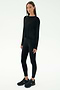 A woman faces forward against a white background wearing the SPLITS59 Djuna Long Sleeve - Black, paired with black leggings and sneakers—an ideal women's activewear look for cool weather workouts.