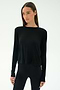 A woman wears the SPLITS59 Djuna Long Sleeve in black, paired with black leggings and standing against a plain light background—ideal women's activewear for cool weather workouts.