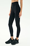 A person wears SPLITS59 Airweight Super High Waist 7/8 leggings in black with black athletic shoes, standing against a plain light background.