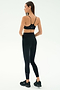 A woman faces away, wearing the SPLITS59 Airweight Super High Waist 7/8 leggings in black, paired with a black sports bra and black sneakers against a plain light background.