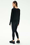 A woman stands on a white background, facing away, wearing the SPLITS59 Djuna Long Sleeve - Black, paired with black leggings and black athletic shoes.