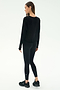 A woman stands on a white background, facing away, wearing the SPLITS59 Djuna Long Sleeve - Black, paired with black leggings and black athletic shoes.