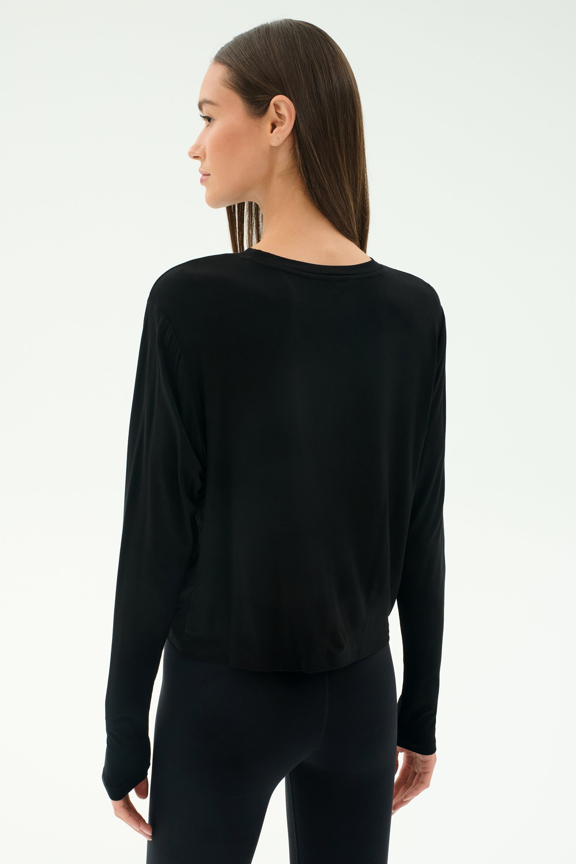 A woman faces away, wearing the SPLITS59 Djuna Long Sleeve in black against a plain light background.