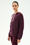 A woman wearing the SPLITS59 Joey Fleece Hoodie in Dark Cherry, featuring white drawstrings and matching leggings, crafted from a soft spandex blend, stands against a plain light background.