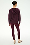 A person is seen from behind, standing against a plain background and wearing the SPLITS59 Joey Fleece Hoodie in Dark Cherry along with matching maroon leggings made from a comfortable spandex blend. Their outfit is completed with beige sneakers accented by maroon stripes.