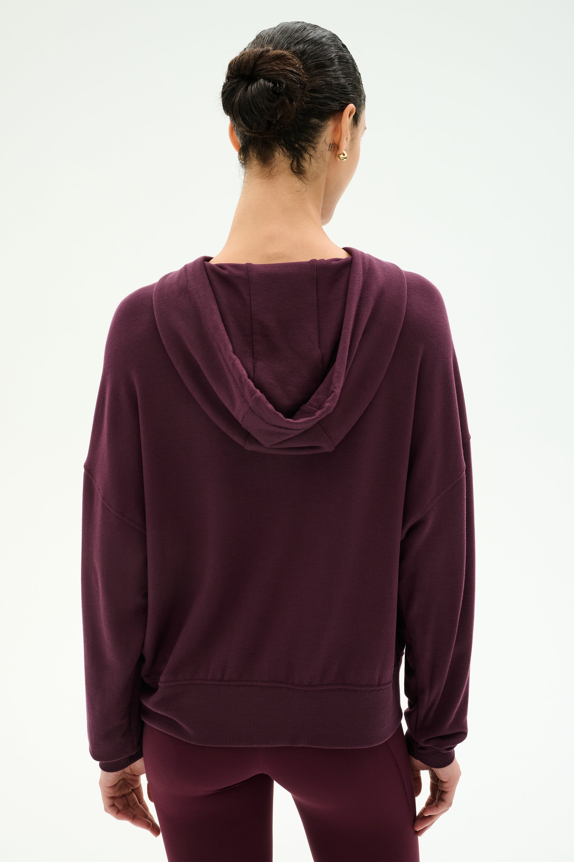 A person with dark hair in a bun is shown from the back against a plain white background, wearing the SPLITS59 Joey Fleece Hoodie in Dark Cherry paired with matching leggings.