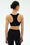 A woman with dark hair in a bun is seen from behind, wearing the SPLITS59 Lexi Rigor Bra in Black/Dark Chocolate and matching leggings—an ideal gym outfit—set against a simple light background.