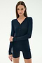 A woman stands against a plain background wearing the SPLITS59 Louise Rib Henley in Indigo with matching navy shorts.