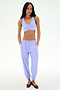 A woman stands against a plain background wearing the SPLITS59 Megan Woven Nylon Jogger in Purple Haze and a matching sports bra, paired with black flats, her hands in her pockets.