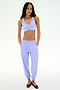 A woman stands against a plain background wearing the SPLITS59 Megan Woven Nylon Jogger in Purple Haze and a matching sports bra, paired with black flats, her hands in her pockets.
