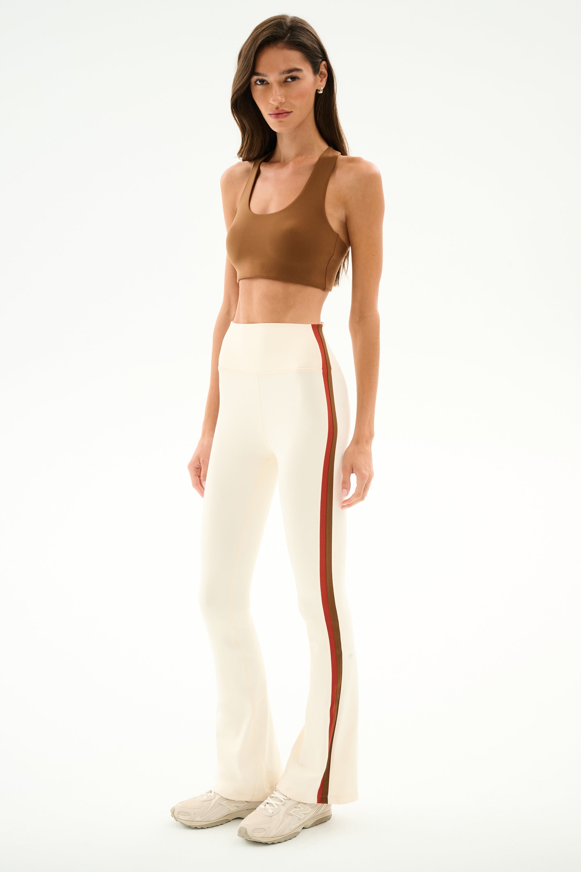 A person wearing a brown sports bra and the SPLITS59 Raquel High Waist Supplex Flare - Creme/Terracotta leggings with side stripes.