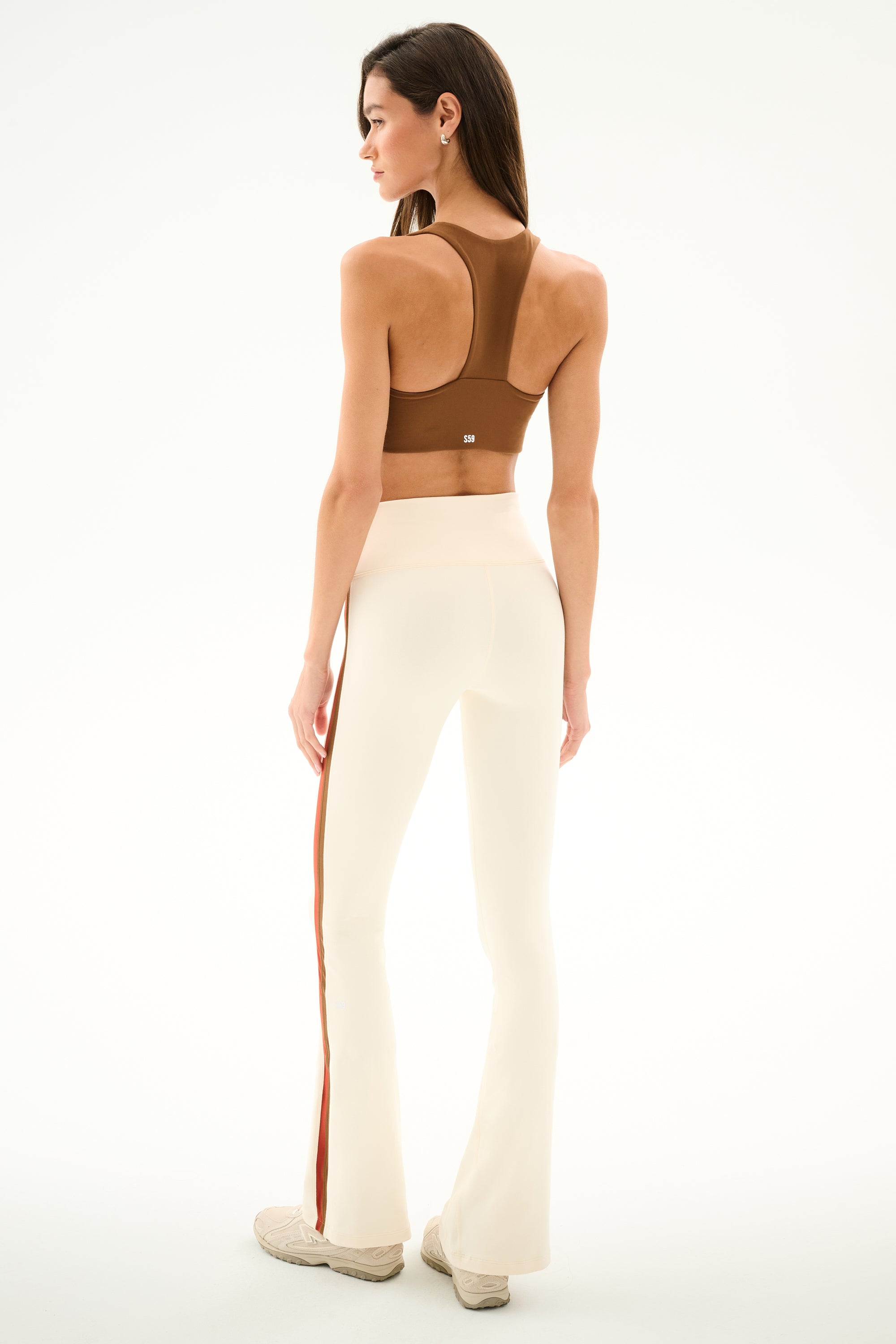 A person seen from behind wears a brown racerback sports bra and Raquel High Waist Supplex Flare - Creme/Terracotta leggings with a terracotta stripe down the leg.