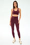 A woman stands against a plain background wearing the SPLITS59 Sara Airweight Bra in Dark Cherry paired with matching high-waisted leggings and light-colored sneakers.