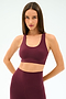 A woman wears the SPLITS59 Sara Airweight Bra in Dark Cherry, paired with high-waisted leggings, both crafted from soft nylon-spandex fabric, standing against a plain light background.
